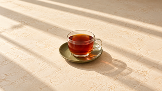 Glaskop med rødbrun rooibos på en grøn underkop på et lyst bord i sollys