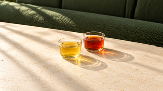 To glas te i sollys på et lyst bord, et med lys gylden te og et med mørk rødbrun te